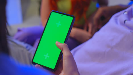 Close-Up-Of-Woman-With-Green-Screen-Mobile-Phone-Sitting-With-Gen-Z-Friends-Talking-And-Sharing-Posts-8